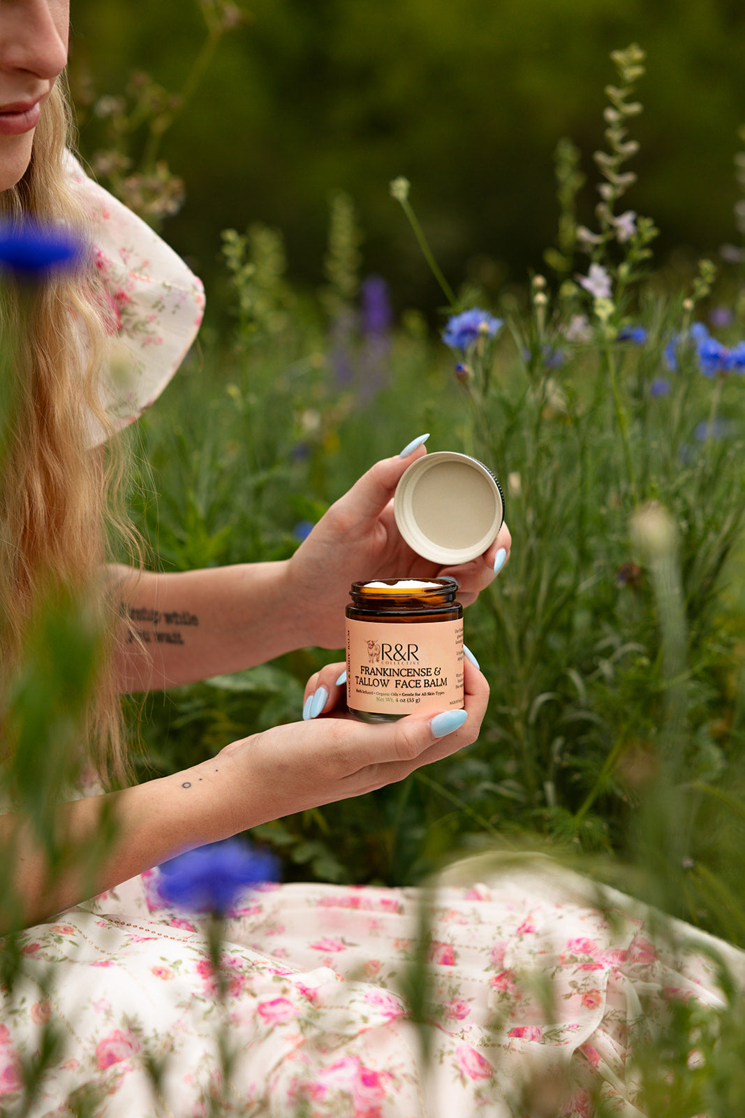 Opening a jar of Frankincense & Tallow Face Balm in a wildflower meadow